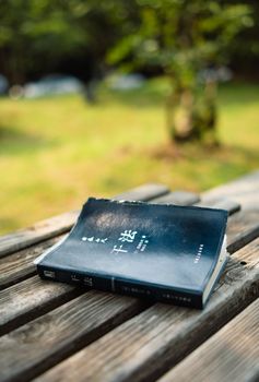 A book lies on a wooden bench outdoors, basking in natural sunlight.