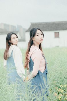 Two young women holding hands in a tranquil field, symbolizing friendship and beauty.