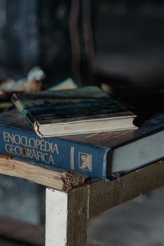 A close-up view of books, including an encyclopedia, resting on a rustic table in dim light.