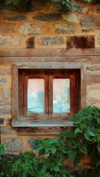 A rustic wooden window set in a stone wall surrounded by green plants in Istanbul, Türkiye.