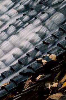 Close-up of flowing water over roof tiles with autumn leaves, creating a serene natural scene.