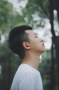 Profile of a relaxed young man outdoors, surrounded by softly blurred greenery.