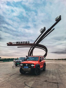 A vibrant red SUV parked near a large, winding sculpture with sky in the background.