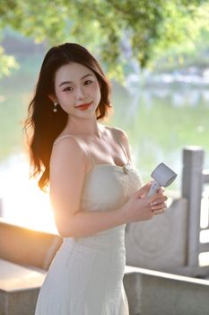 Elegant young woman in a summer dress enjoys sunlight in a serene outdoor setting.
