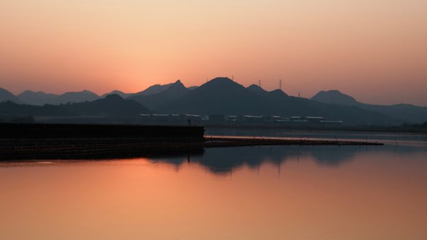 Serene sunset over a calm lake with mountains in the background, creating a beautiful reflection.