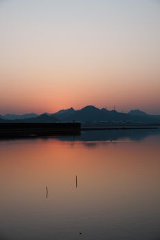 A serene scene of a sunset over a distant mountain range reflected in calm water.