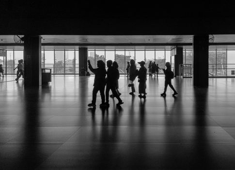 Silhouettes of people walking in an indoor Jakarta station, shot in black and white.