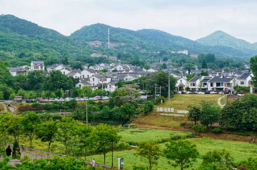 Picturesque Chinese village surrounded by verdant hills under a cloudy sky.