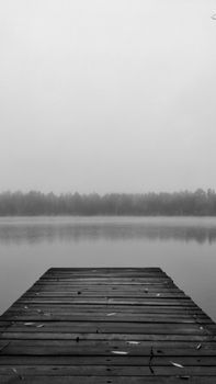Serene grayscale view of a wooden dock leading into a misty lake surrounded by trees.