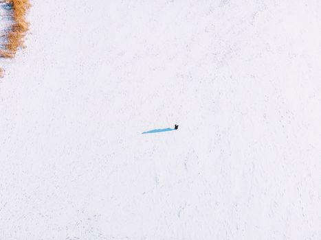 Aerial shot of a solitary figure on a vast snowy field in Harbin, China, capturing winter's stark beauty.