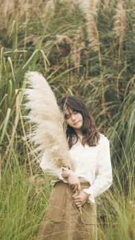 A serene portrait of a woman holding pampas grass in a lush green field.