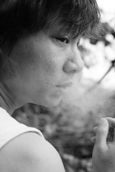 Introspective black and white portrait of an Asian man smoking, capturing a thoughtful moment.