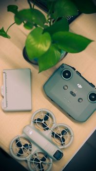 Drone controller and accessories with green plant on a desk, minimal tech setup.