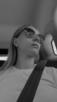 Stylish woman wearing sunglasses, sitting in a car, monochromatic style.