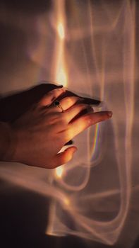 A hand adorned with a ring interacting with an artistic rainbow reflection on a wall.