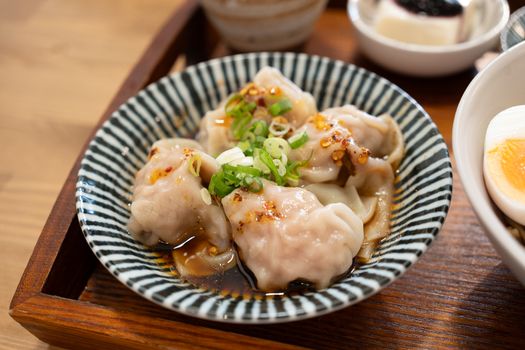 Close-up of savory dumplings with soy sauce, scallions, and chili oil, served on a striped ceramic plate.