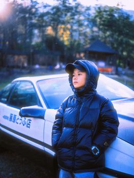 A child in a winter coat leans against a classic car outdoors in Dali, China.