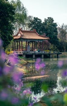 Traditional pavilion beside a tranquil pond with lush foliage in Nanjing, China.