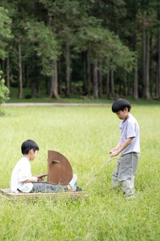 Two boys engaged in imaginative play in a grassy field, pulling a handmade wooden cart.