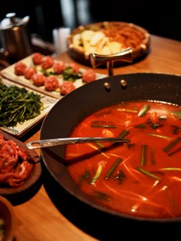 Delicious spicy hotpot with assorted ingredients on a wooden table, perfect for Asian cuisine enthusiasts.