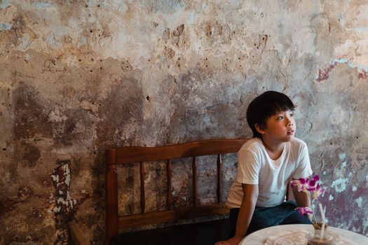 A young boy in a white shirt seated on a wooden bench, gazing away in a rustic setting.