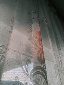 From below of white tulle curtain with flower pattern on window in bright sun lit room of house