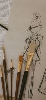 Close-up of a fashion sketch with paintbrushes on paper, showcasing creativity.