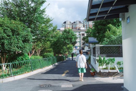 Young woman walking down a leafy street under bright summer sunlight.