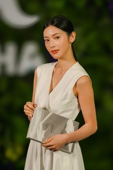 Elegant woman in white dress holding a book at an event in Taipei, showcasing sophisticated style.