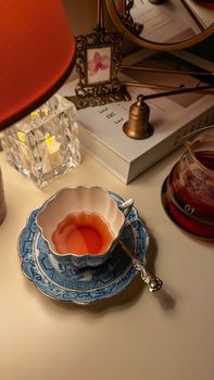 A cozy scene featuring a blue porcelain teacup, a glass tea warmer, and ambient lighting creating a warm atmosphere.