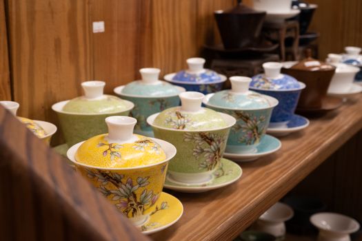 An array of colorful, traditional teacups with intricate floral designs displayed on a wooden shelf.