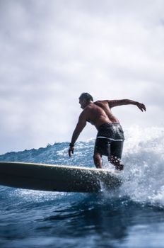 Male surfer riding ocean waves with a surfboard on a bright sunny day.