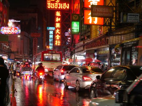 A lively night scene in Bangkok's Chinatown with busy traffic and illuminated neon signs.