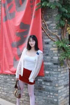 Stylish woman leaning against a brick wall in Nanjing, China, with red banner.